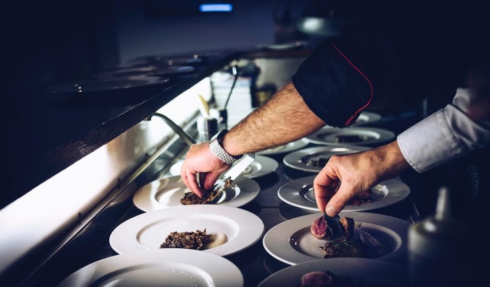 Un cocinero emplatando varios platos en la línea de una cocina.